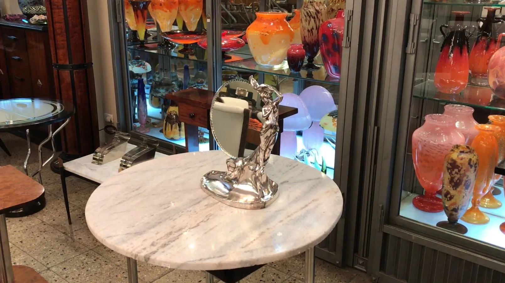 Antique mirror with statue base, stylized decoration, background with colorful vases.