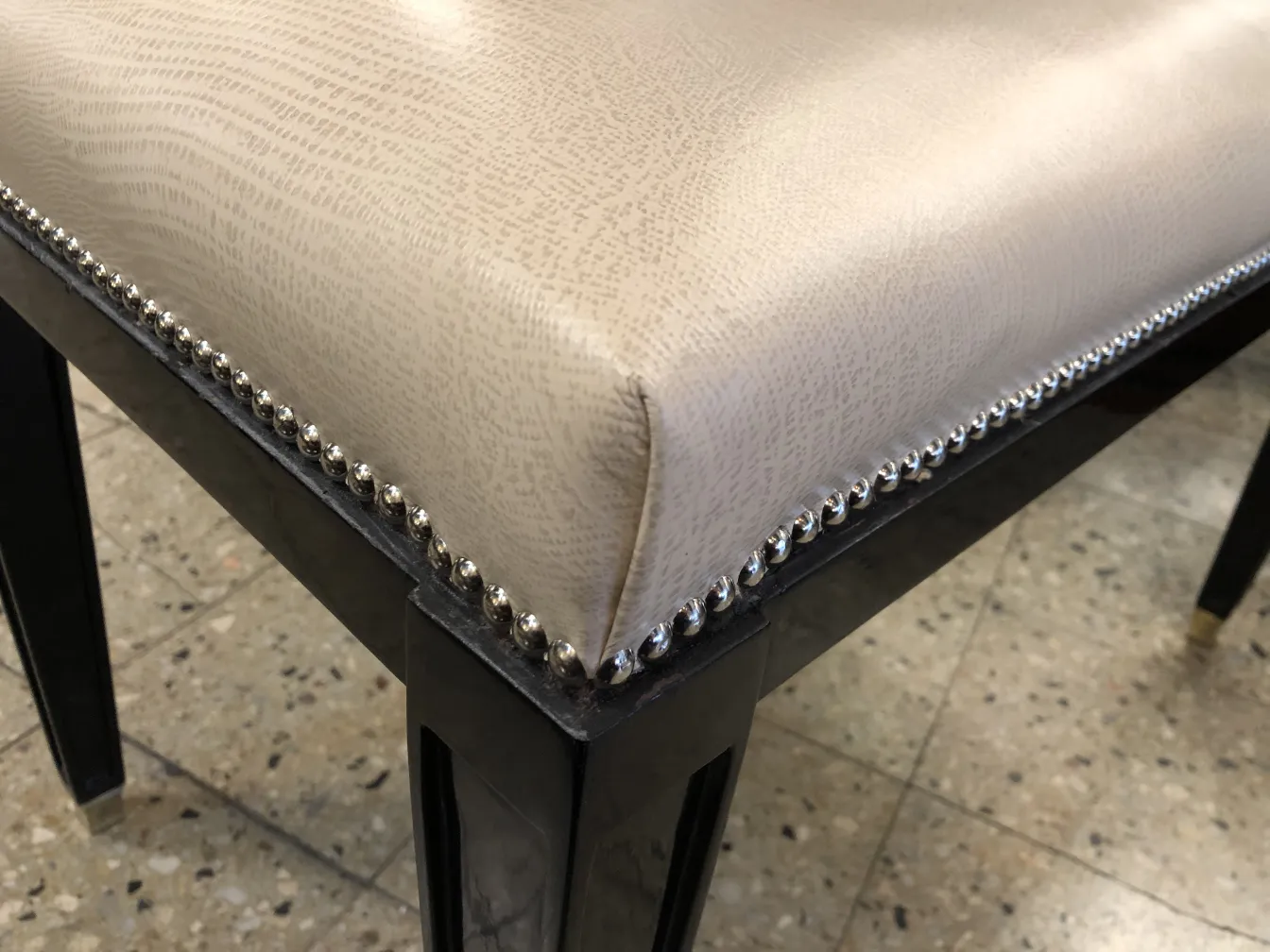 Vista laterale di un antico sgabello con rivestimento beige e dettagli metallici in un ambiente classico.