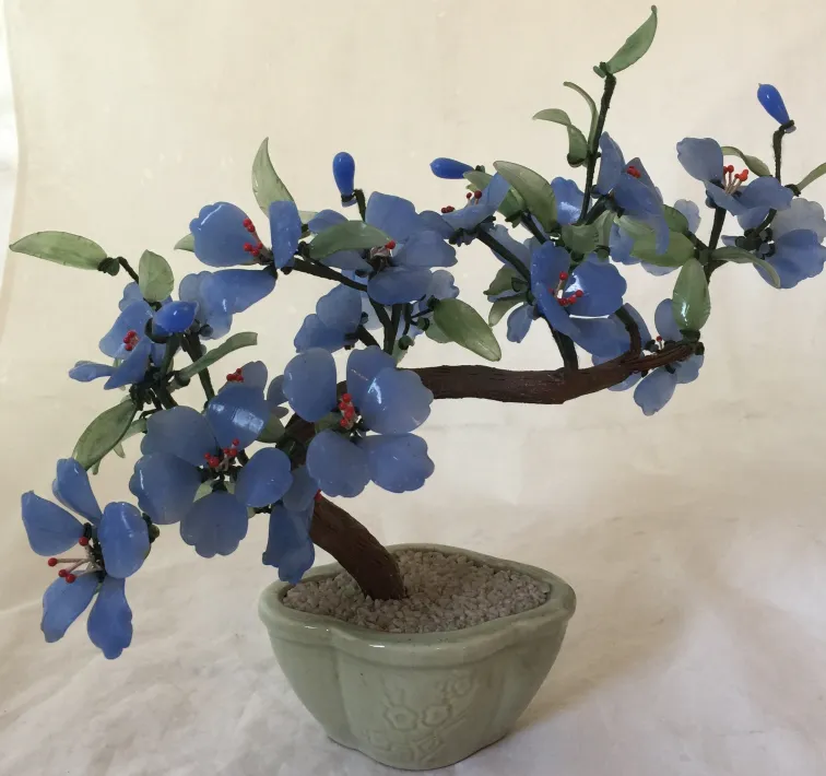 Antique bonsai with blue flowers and green leaves in decorative pot
