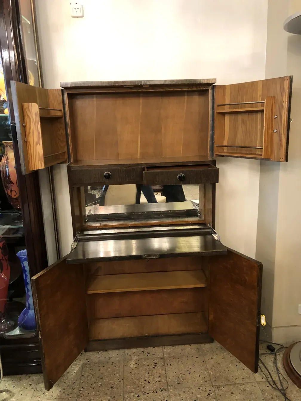 Antique wooden bar cabinet with a mirror on top, opened with interior shelves.