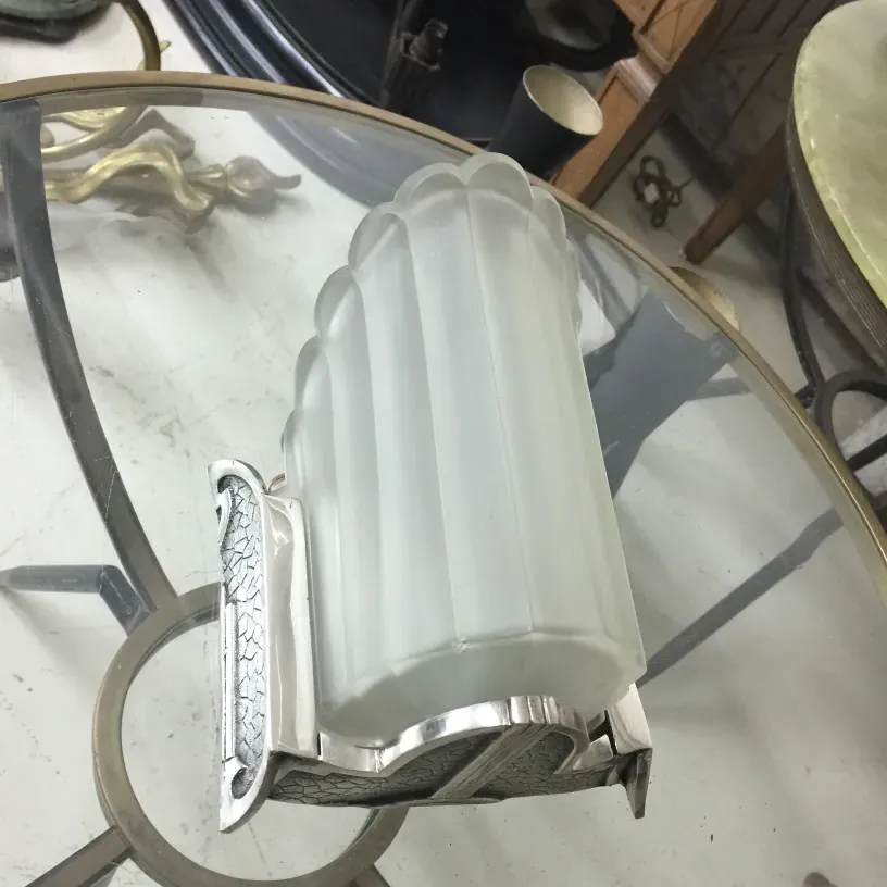 Antique pair of sconces featuring detailed base and frosted glass, in a setting with various furniture.