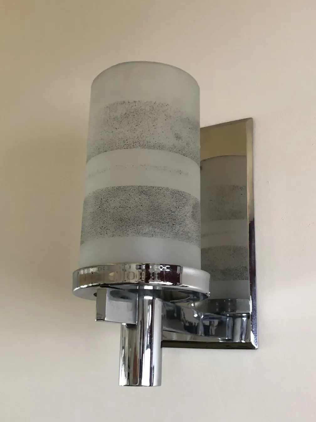 Pair of cylindrical sconces with metal detailing, illuminating a light wall.