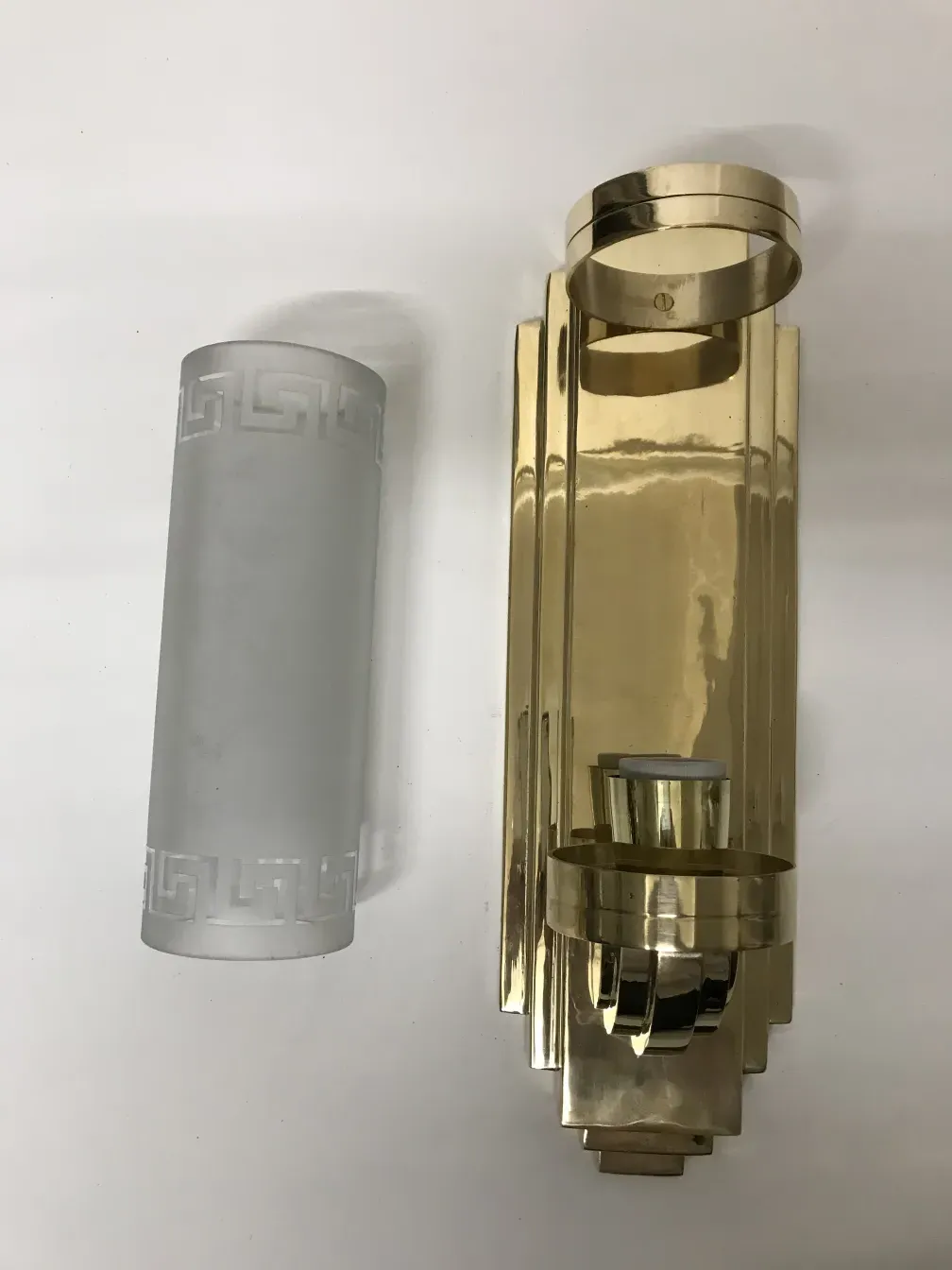 Antique pair of sconces featuring elegant geometric design, one in a shiny gold finish and the other with a glass diffuser. Warm ambient lighting.