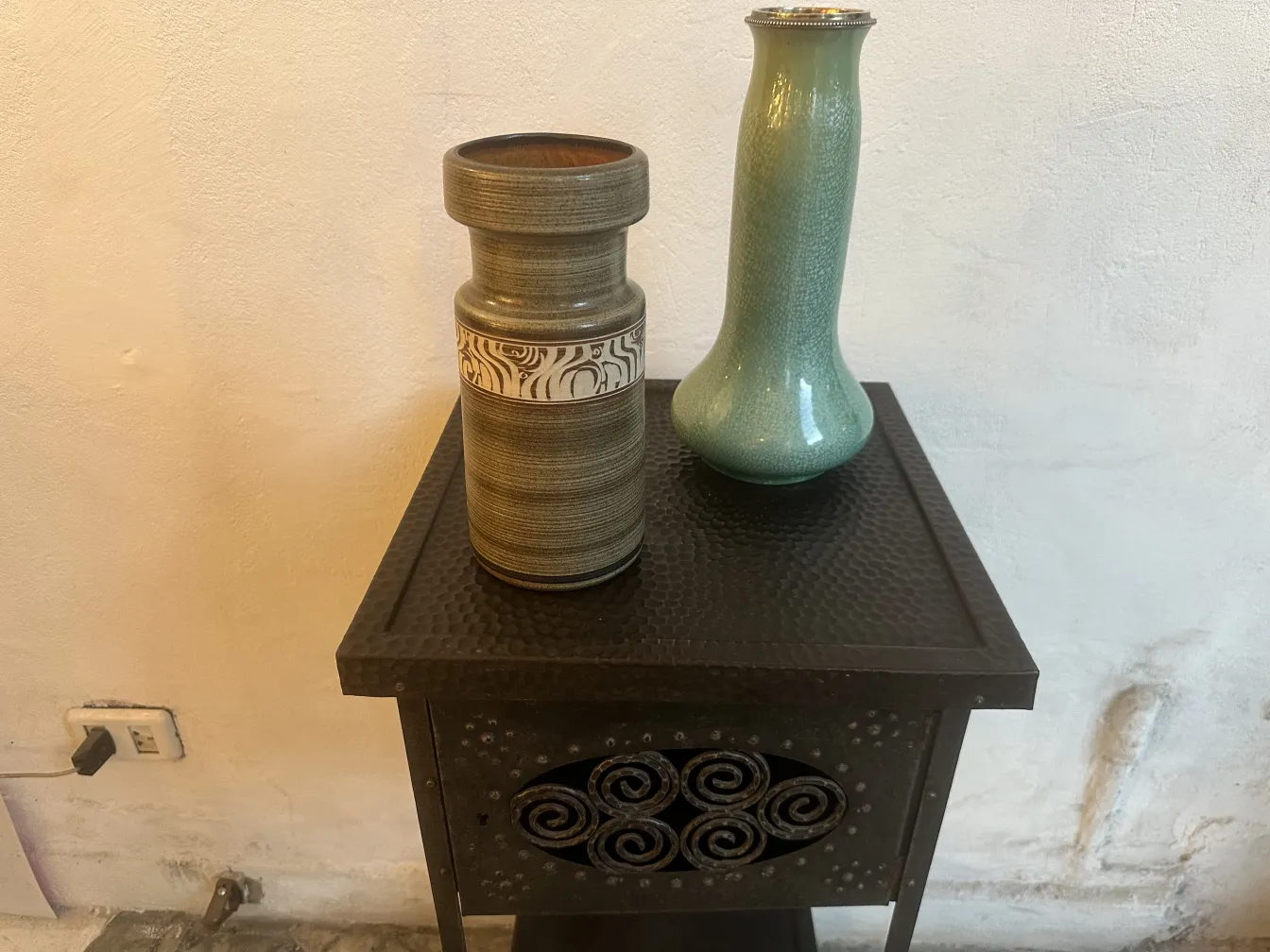 Two antique ceramic vases on a black table, one green and the other with a pattern