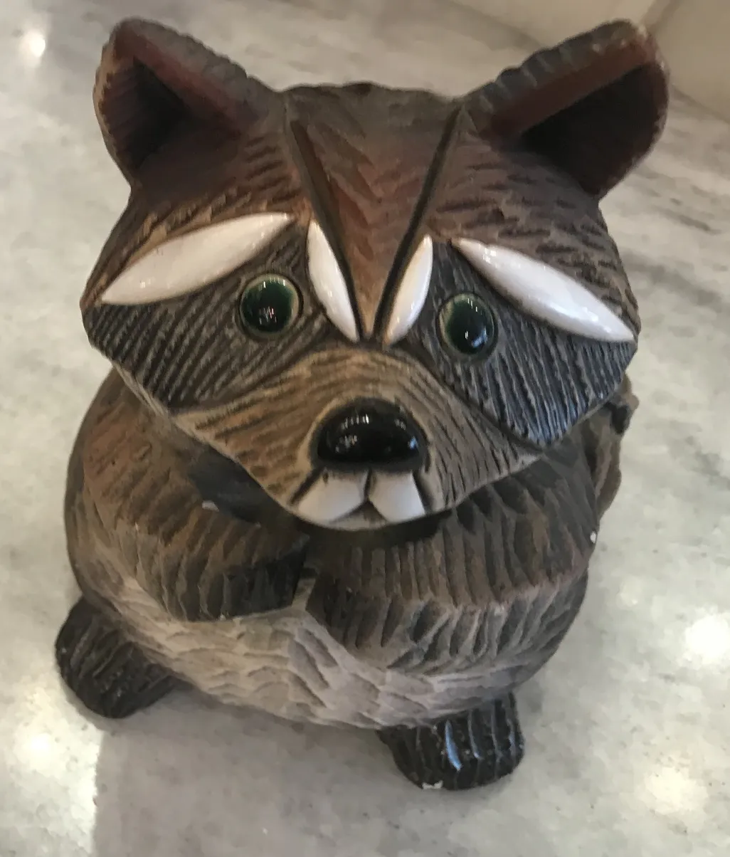 Antique ceramic sculpture depicting a raccoon with green and brown details on a light surface.