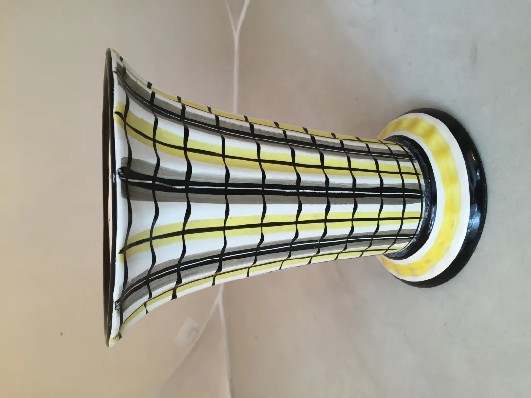 Antique ceramic vase featuring a black and white pattern with yellow details, set on a light surface.