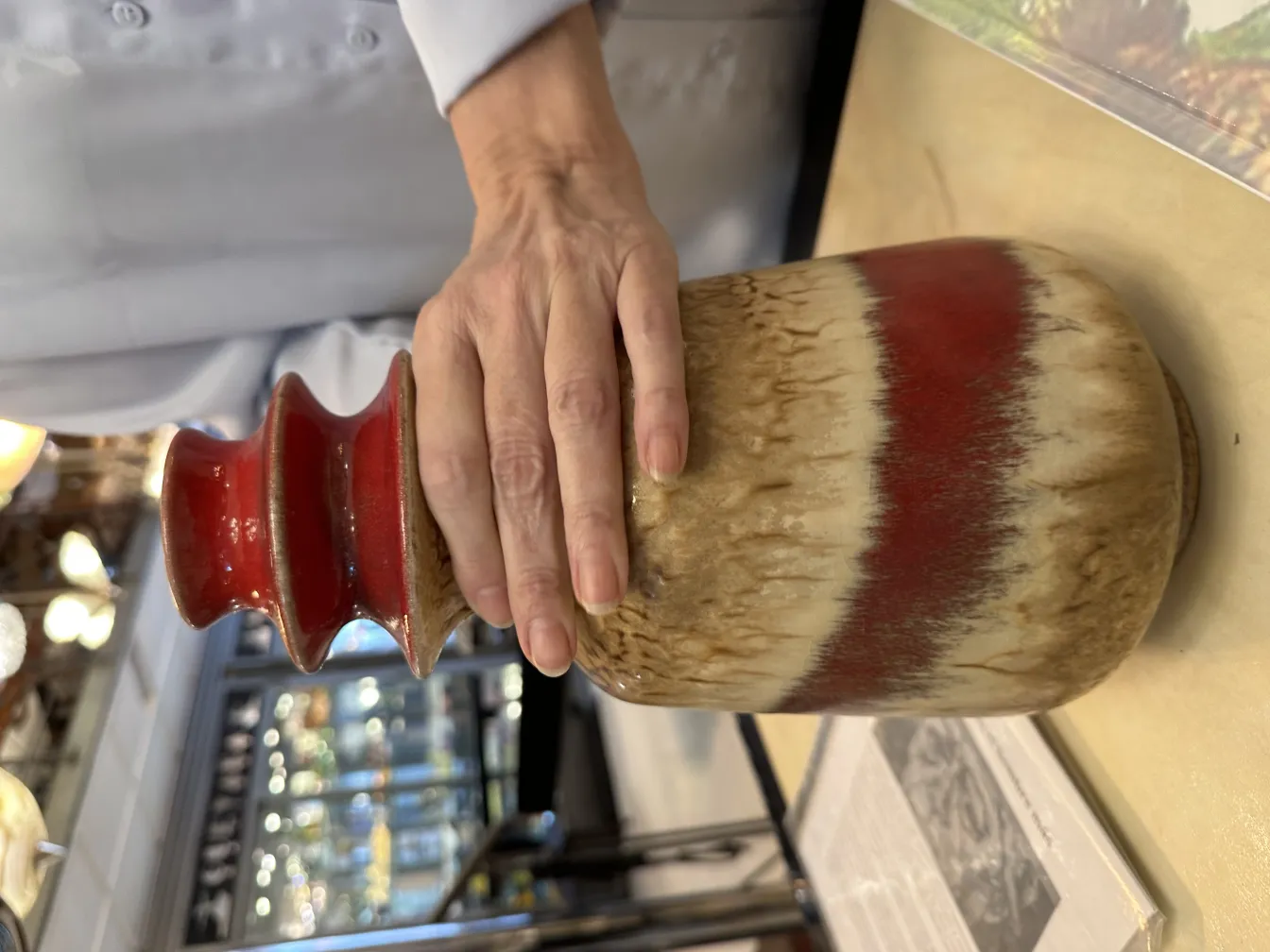 Antique ceramic jar with multicolor design and irregular texture, held by a hand.