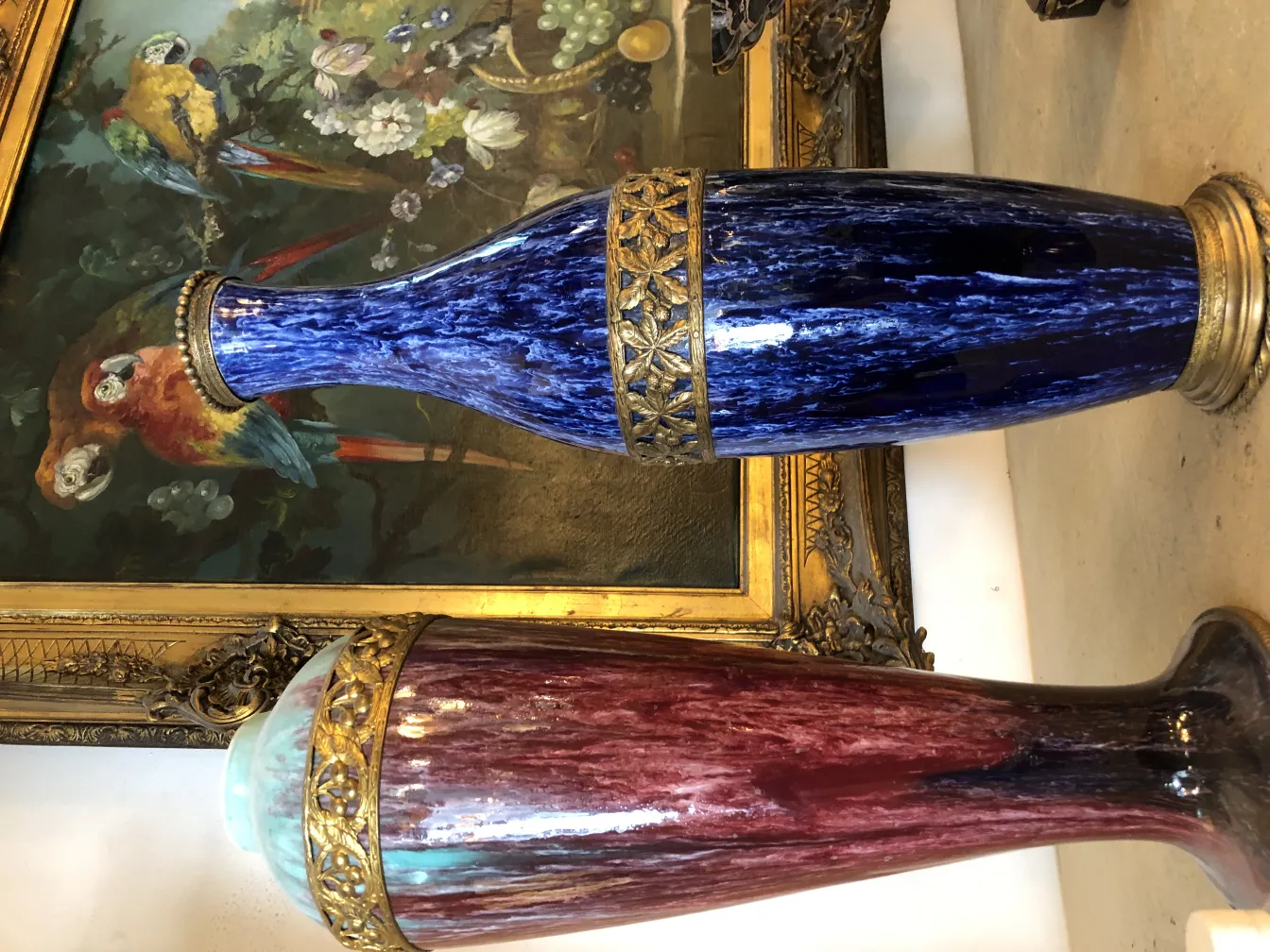 Antique blue and red ceramic vases, adorned with golden details, backdrop includes a painting of parrots.