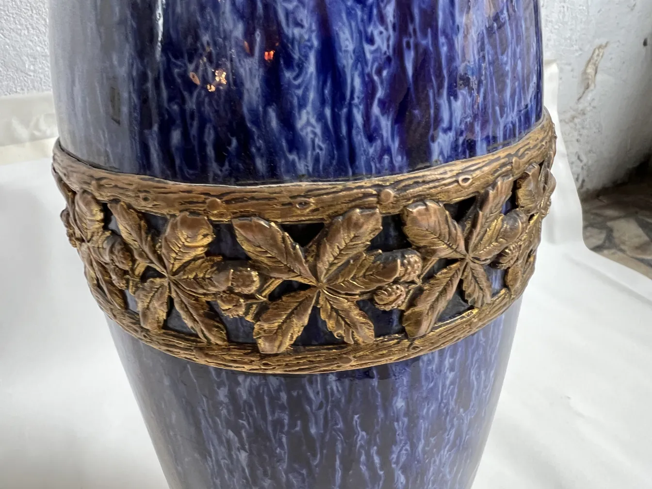 Antique blue ceramic vase with a golden relief design around the central part, in a neutral setting.