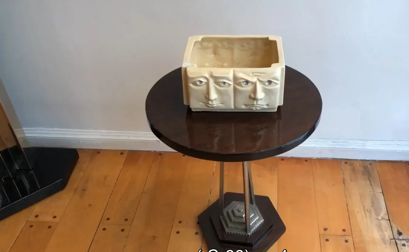 Rectangular antique ceramic container with sculpted faces, placed on a dark table.