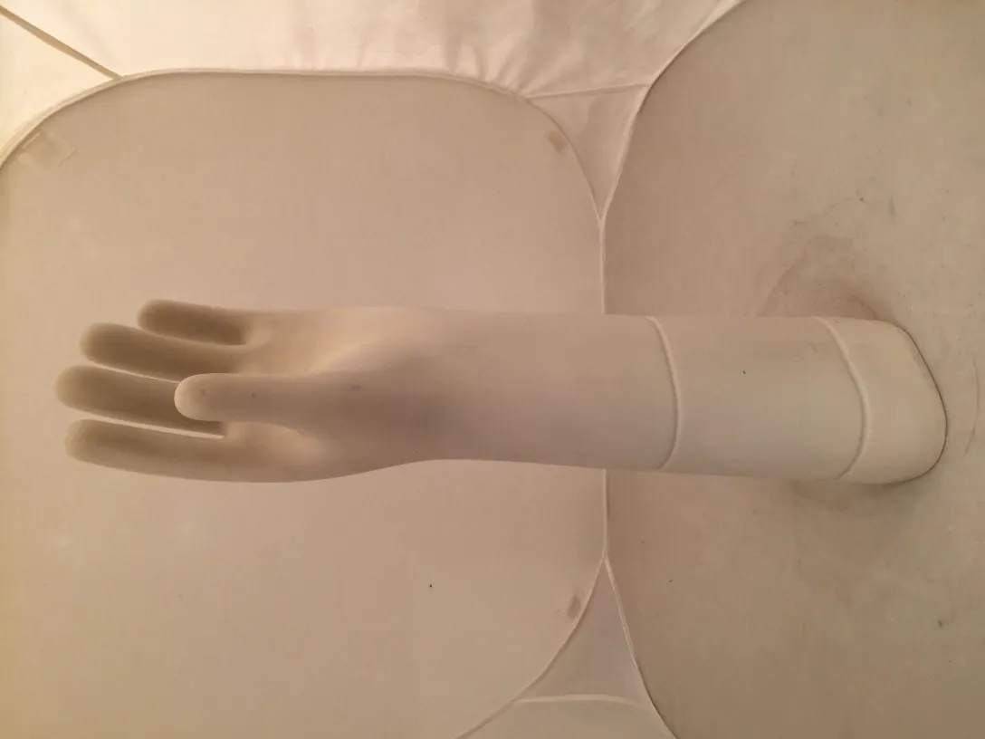 White ceramic hand on antique display against a neutral background.