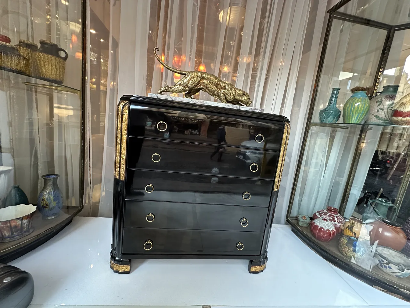 Antique black cabinet with golden details, surrounded by antiques.