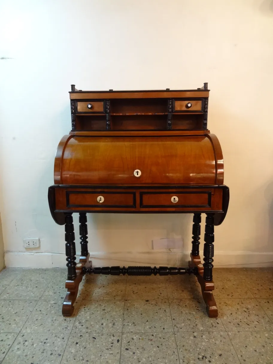 पुरानी लकड़ी की डेस्क जिसमें शेल्फ और सजावटी दराज हैं, साधारण वातावरण में।