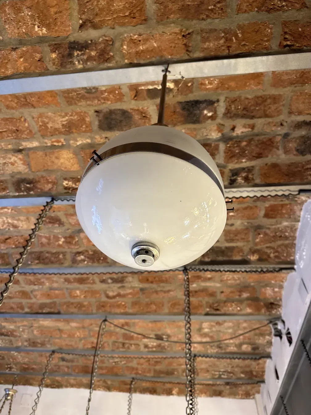 Antique white hanging lamp suspended in a room with brick walls.
