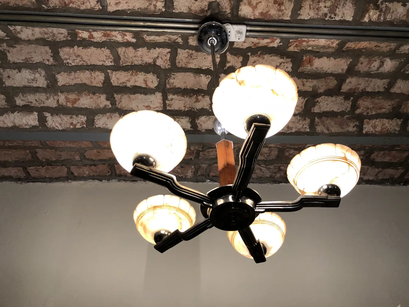 Antique hanging lamp with four bulbs illuminating a space. Exposed brick ceiling.