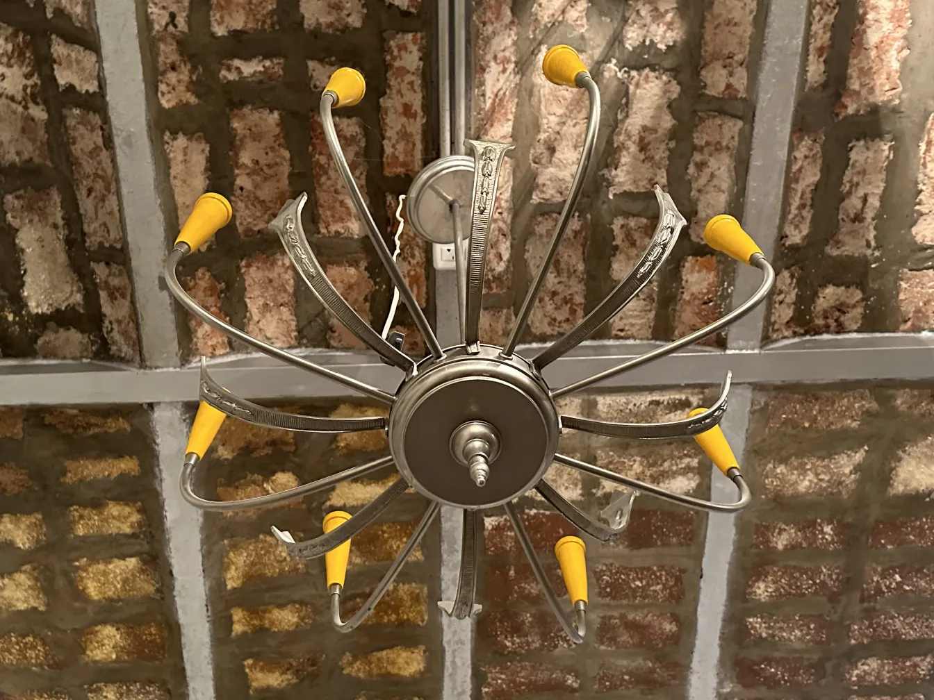 Antique hanging lamp with curved metal arms and yellow details, illuminating a rustic environment.