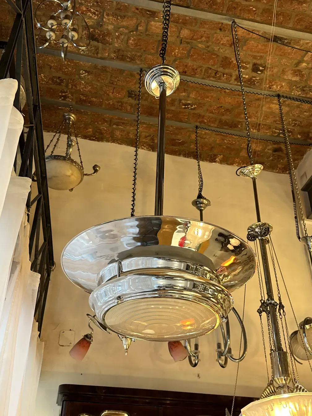 Antique hanging lamp with a glossy design, surrounded by chains and an exposed brick background.