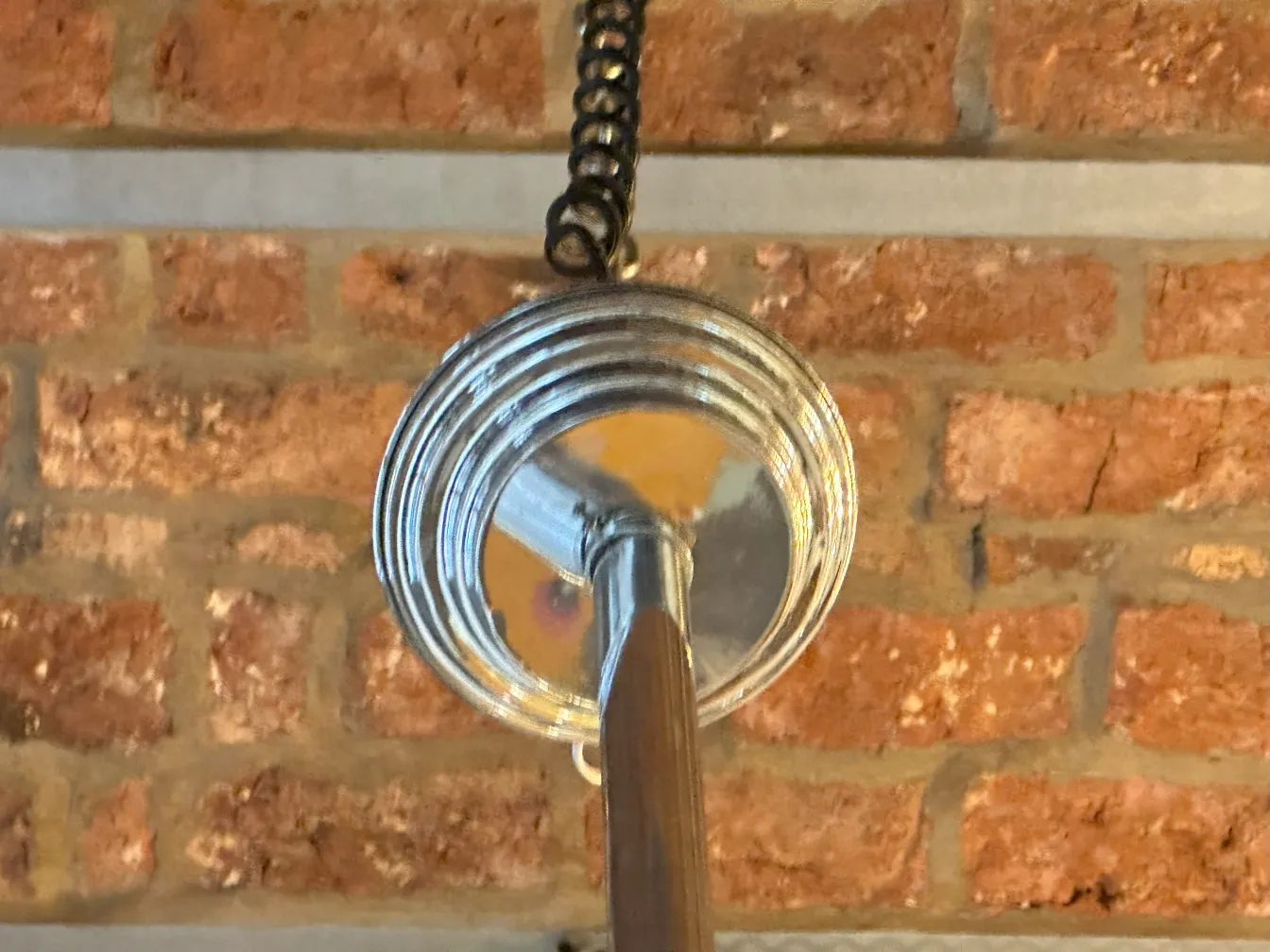 Antique hanging lamp with industrial design, suspended by a wire, against a brick background.