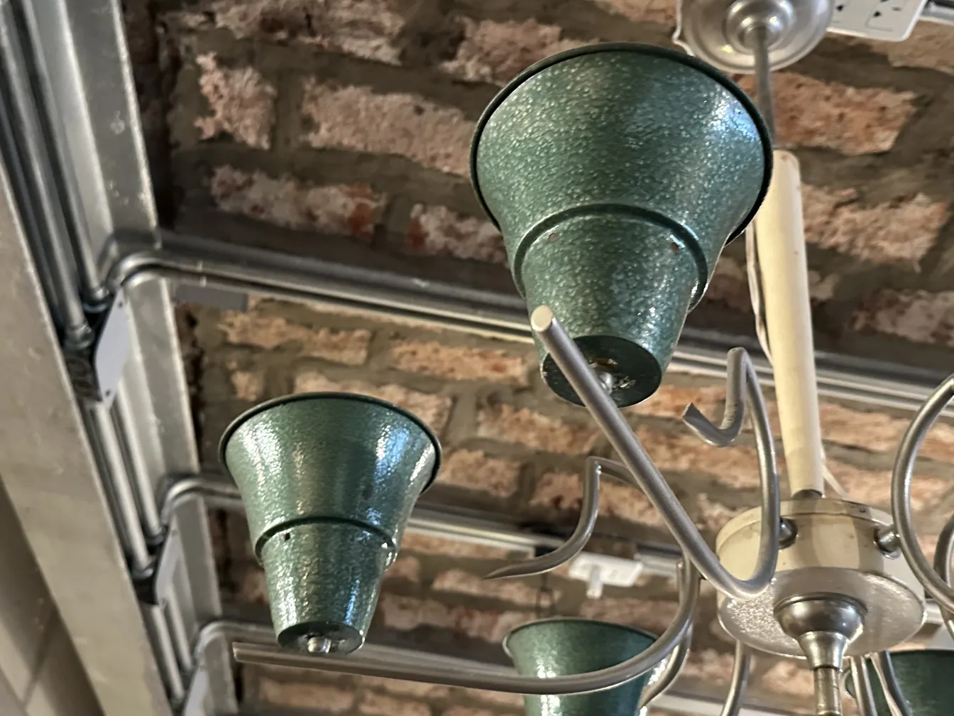 Antique hanging lamp with green shades against a brick background.