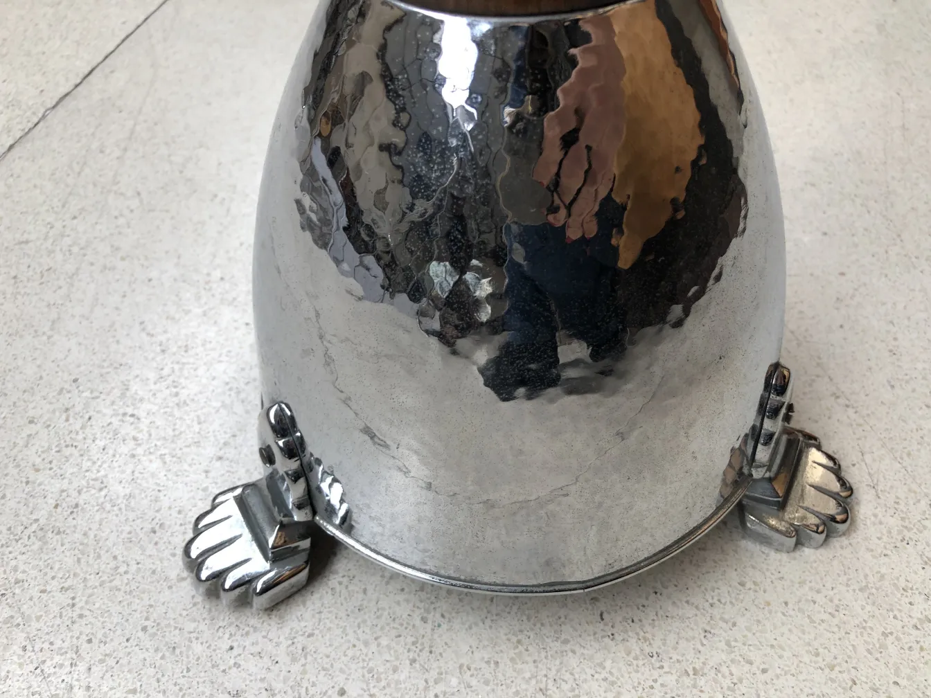 Antique standing ashtray with a shiny finish and decorative feet, on a light surface.