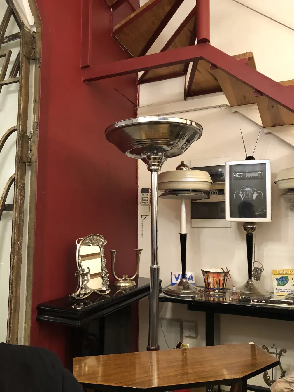 Антикварный торшер с элегантным дизайном в уютной обстановке, с декоративными предметами как стол и коллекционные вещи.