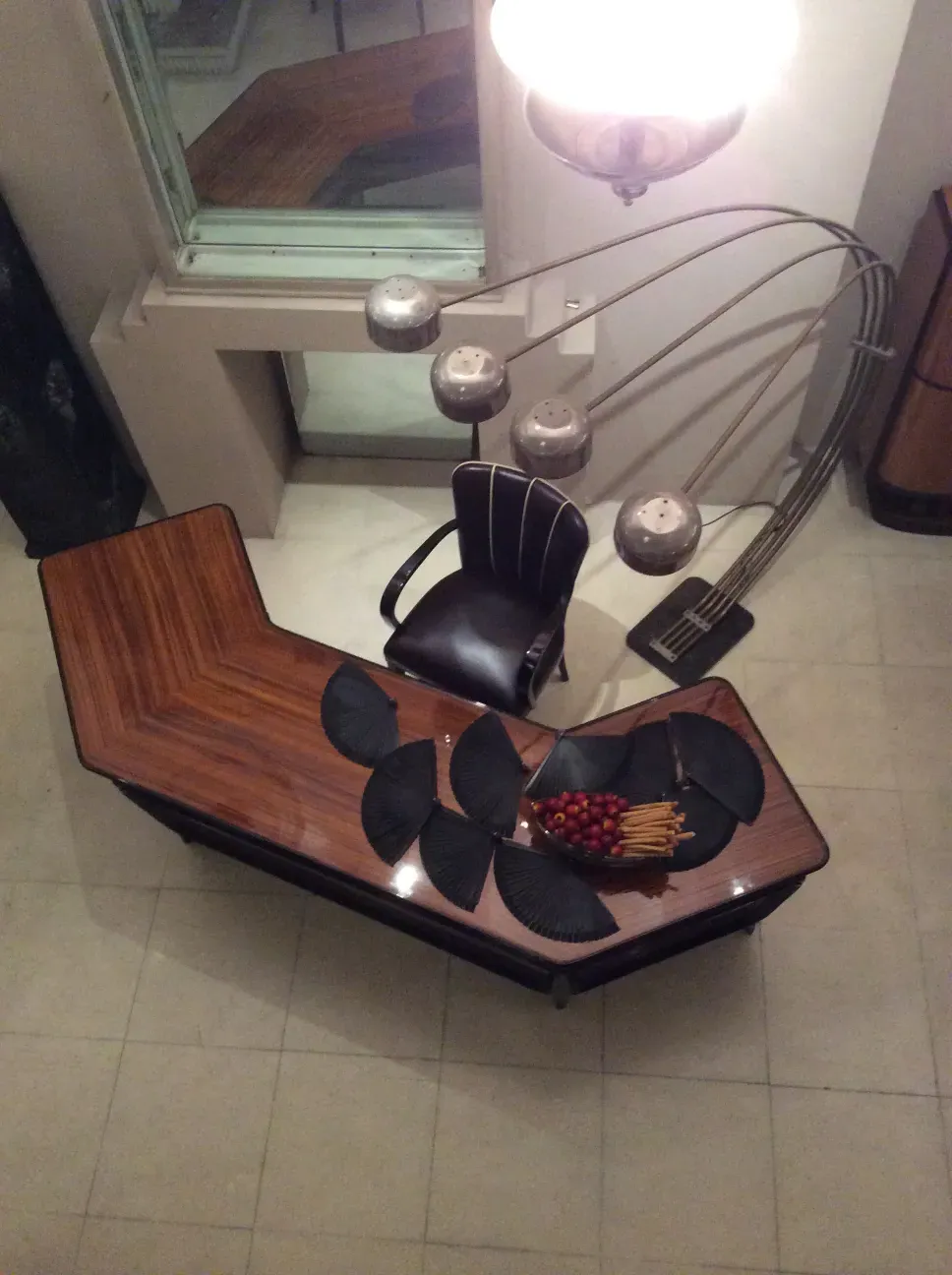 Античный торшер с несколькими светильниками и элегантным дизайном, кресло и стол на заднем плане.