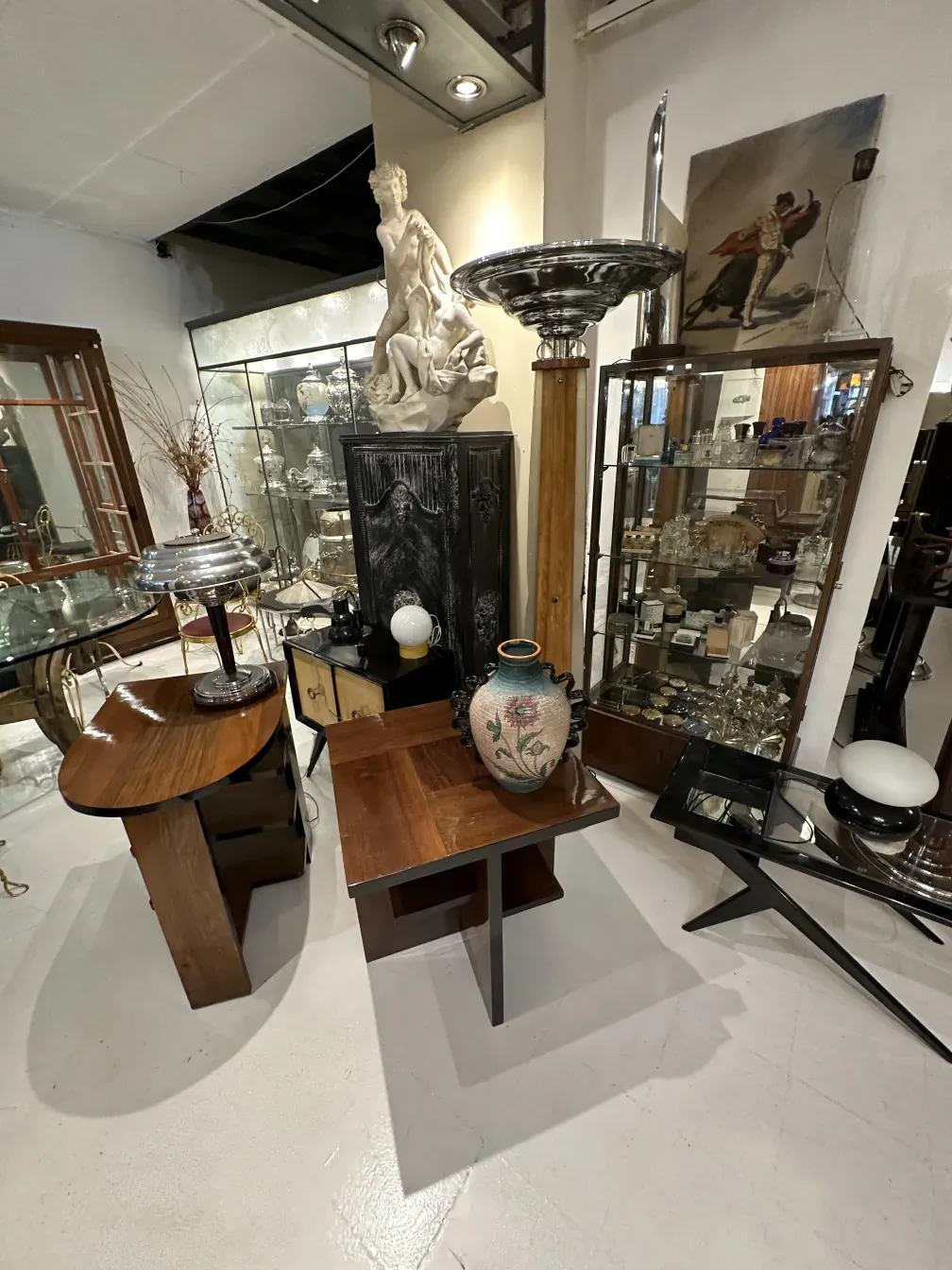 Старый топчан с элегантной основой и белым абажуром, окруженный винтажными украшениями.