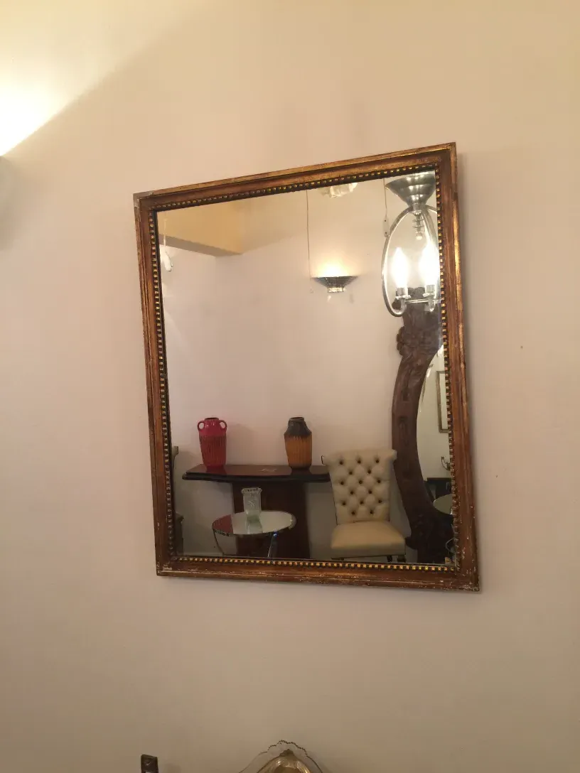 Antique mirror with decorative frame on a white wall, reflecting an elegant setting.