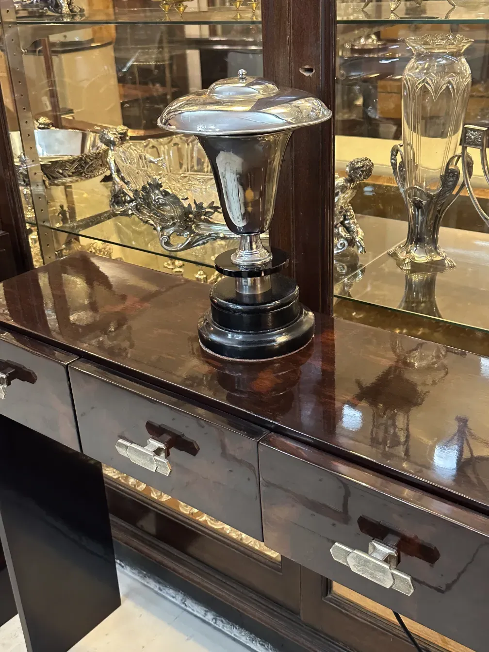 Luminária de mesa antiga com design brilhante e elegante, cercada por outros objetos decorativos.