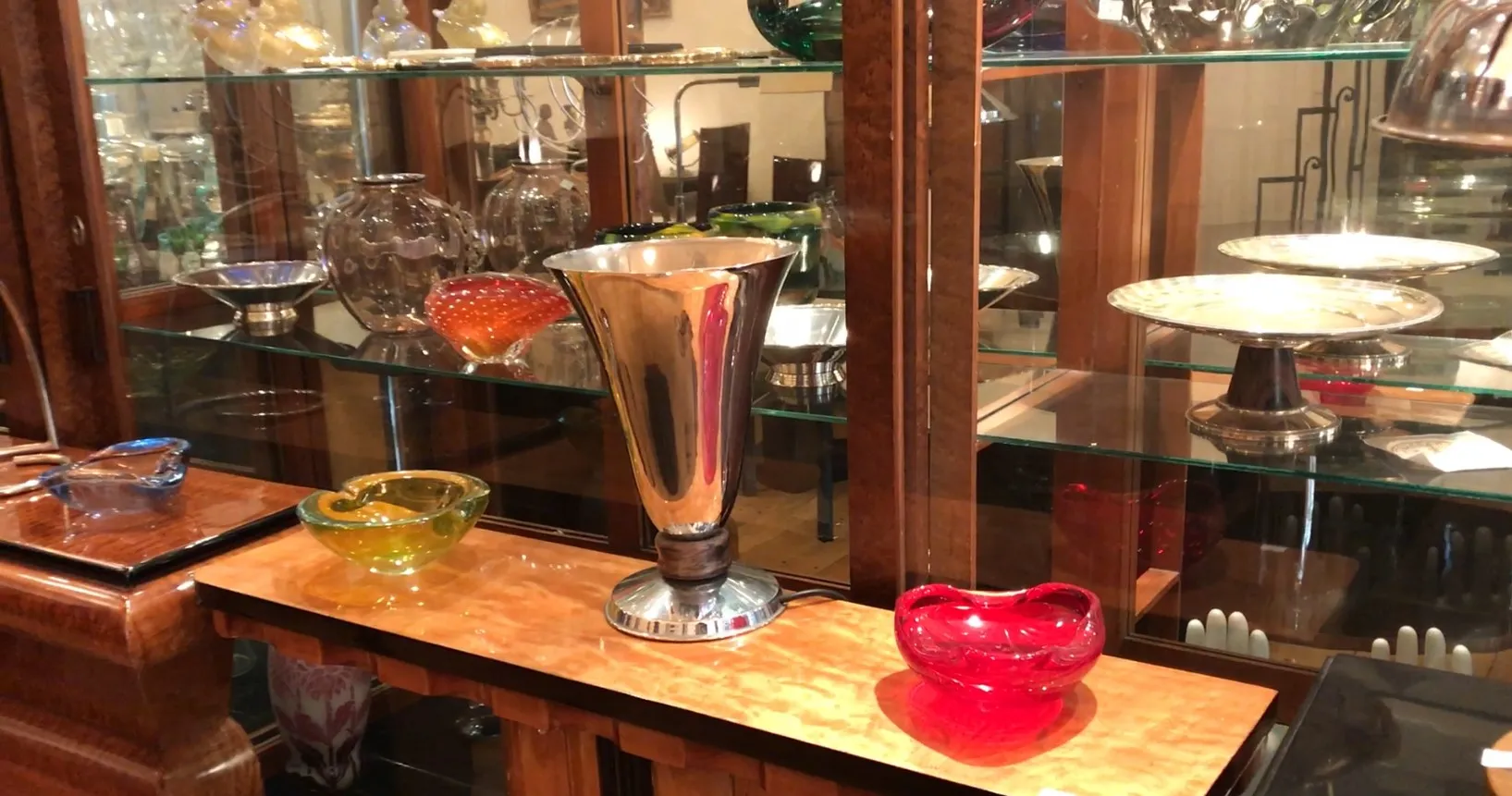 Luminária de mesa antiga com design brilhante, cercada por objetos de vidro em um ambiente elegante.