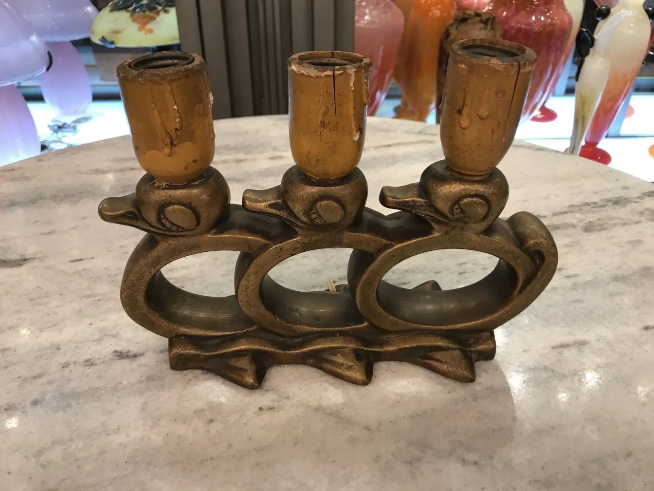 Luminária de mesa antiga com design de três animais em bronze e lâmpadas amarelas, decorando um ambiente iluminado