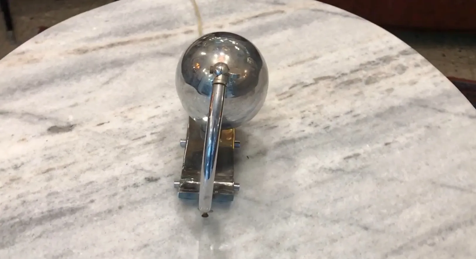 Luminária de mesa antiga com base metálica e esfera brilhante, em uma mesa.