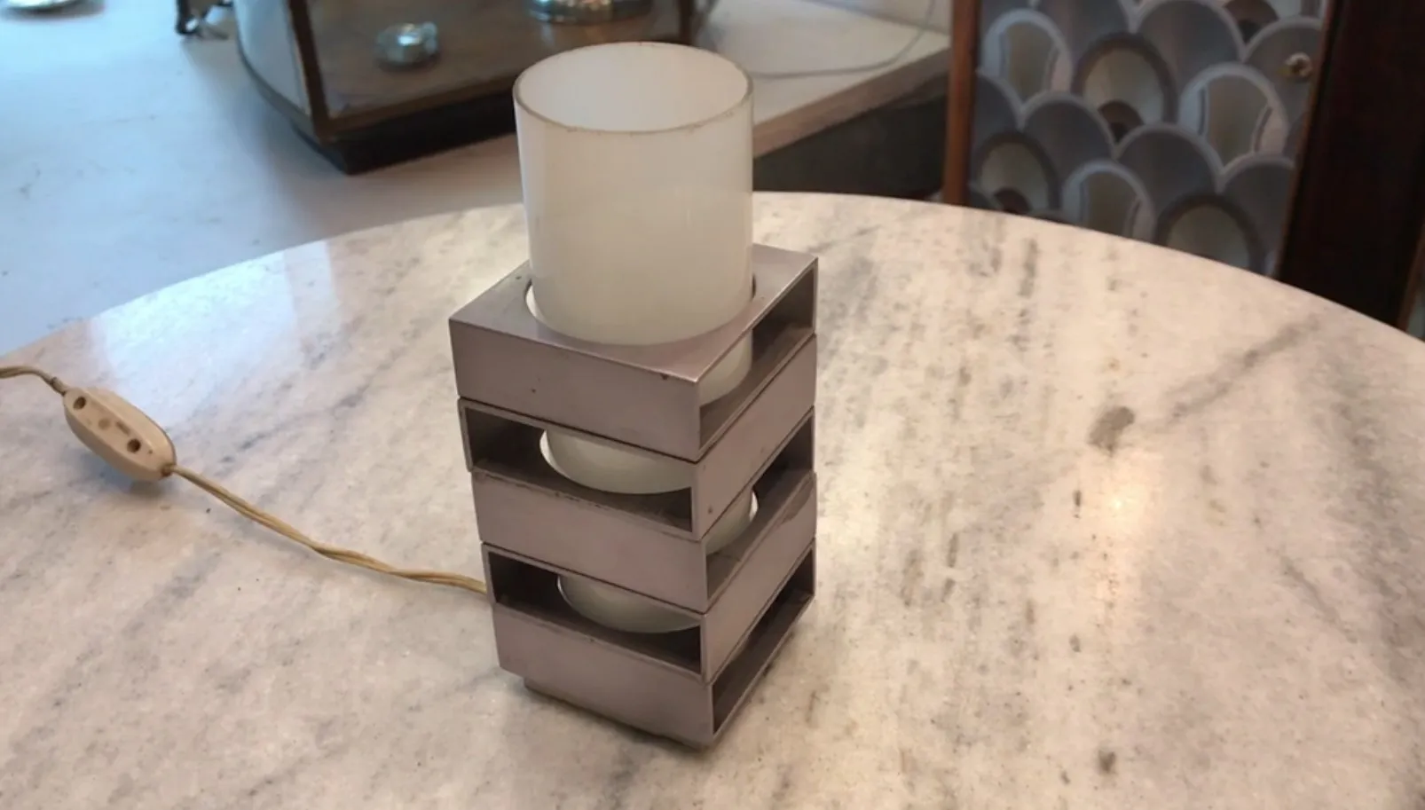 Luminária de mesa antiga com cúpula e base de vidro em uma mesa de mármore.