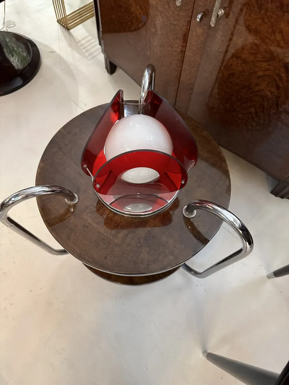 luminária de mesa antiga com base redonda e detalhes vermelhos, ao lado de uma mesa de madeira