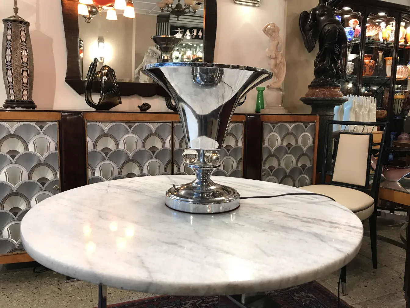 Luminária de mesa antiga com base brilhante em uma mesa de mármore, cercada por decorações.