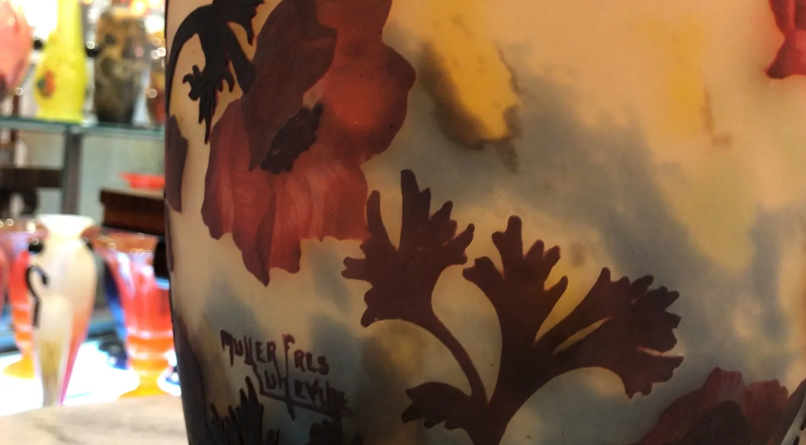 Vidro assinado Muller Fres com desenho floral em tons de amarelo e vermelho, ambiente de antiguidades.