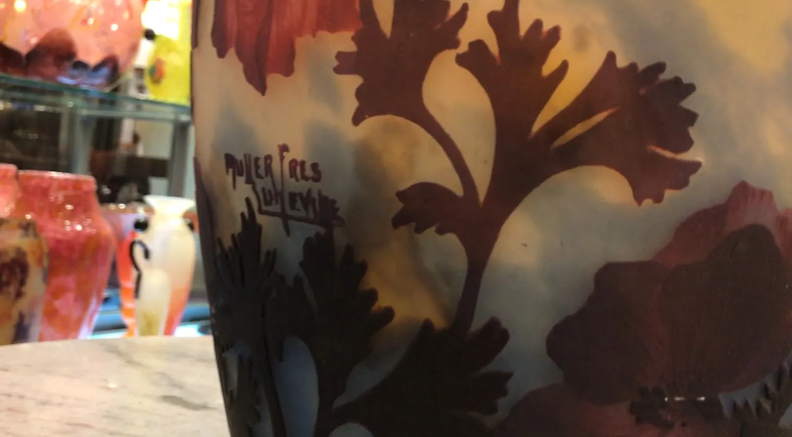 Vidro assinado Muller Freres com design floral em tons quentes, fundo desfocado.