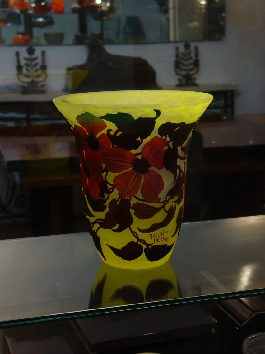 Vaso de vidro com design floral em tons amarelo e vermelho, assinado Muller Freres, exposto em uma vitrine