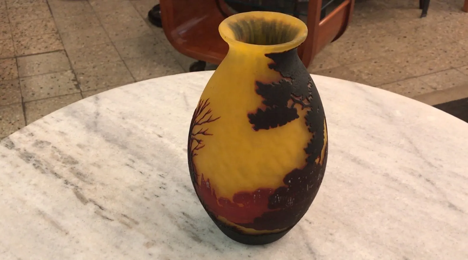 Um elegante vaso de vidro assinado por Muller Fres, com um design decorativo em cores vibrantes sobre um fundo amarelo.