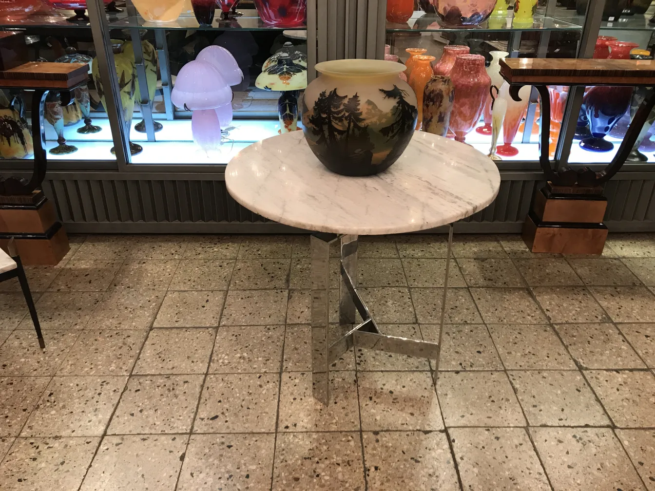 Vidro assinado de Muller Fres exposto em uma vitrine antiga, cercado por outras antiguidades.