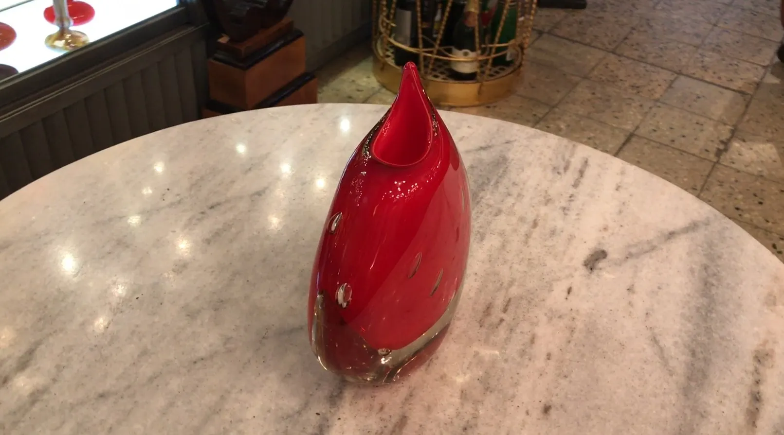 red murano vase with a curvy shape on a marble table, background with decorative items