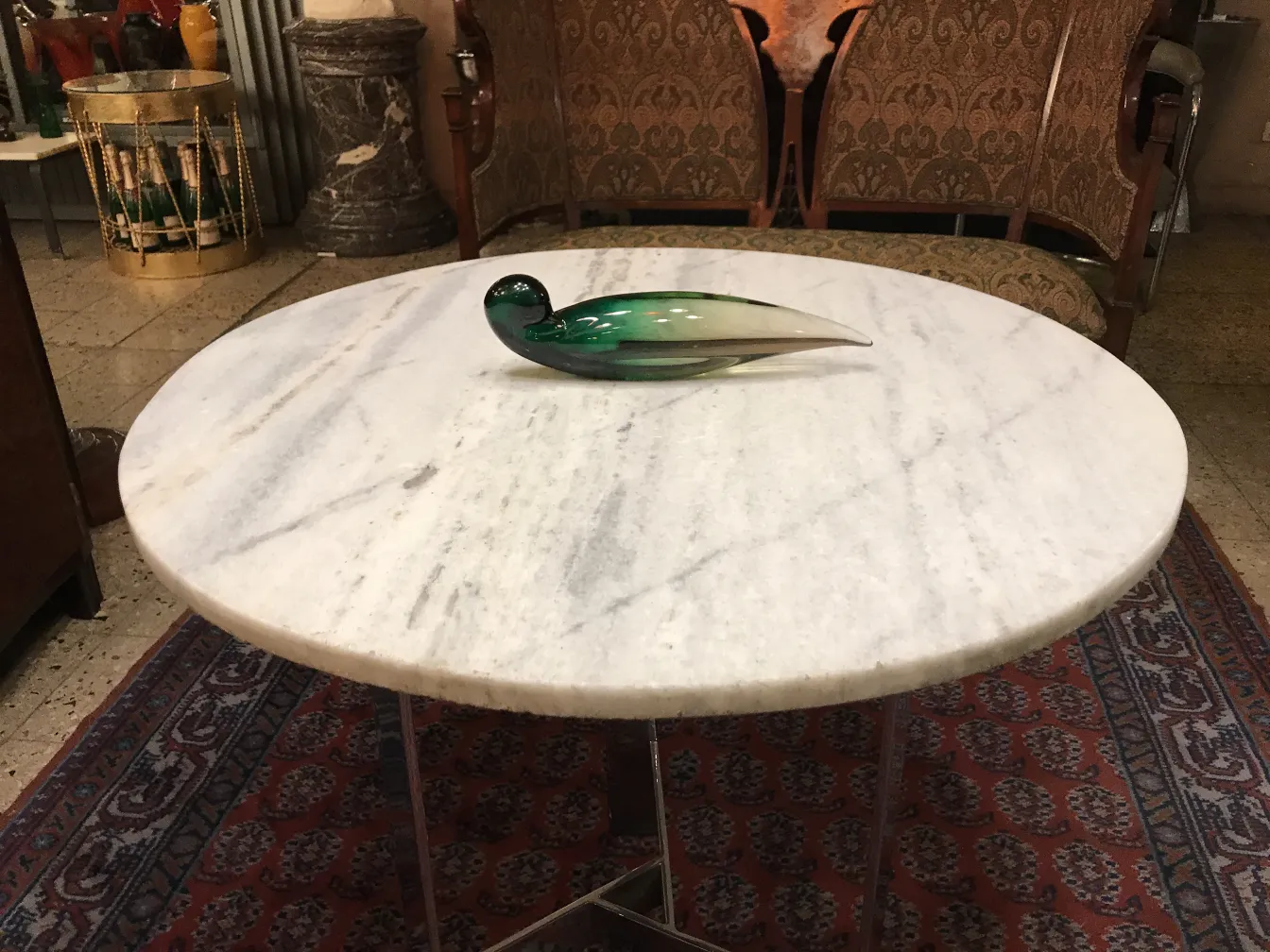 Antique murano glass bird in green color, decorating a marble table