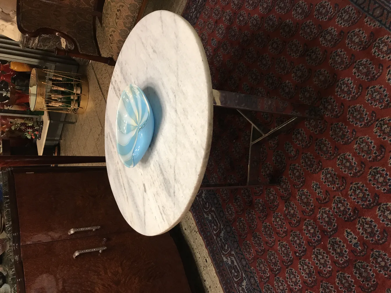 Murano glass bowl in blue tones on a marble table, antique decorations in the background.