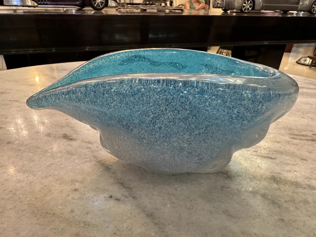 An elegant antique murano glass in blue tone, with organic shape, on a marble table.