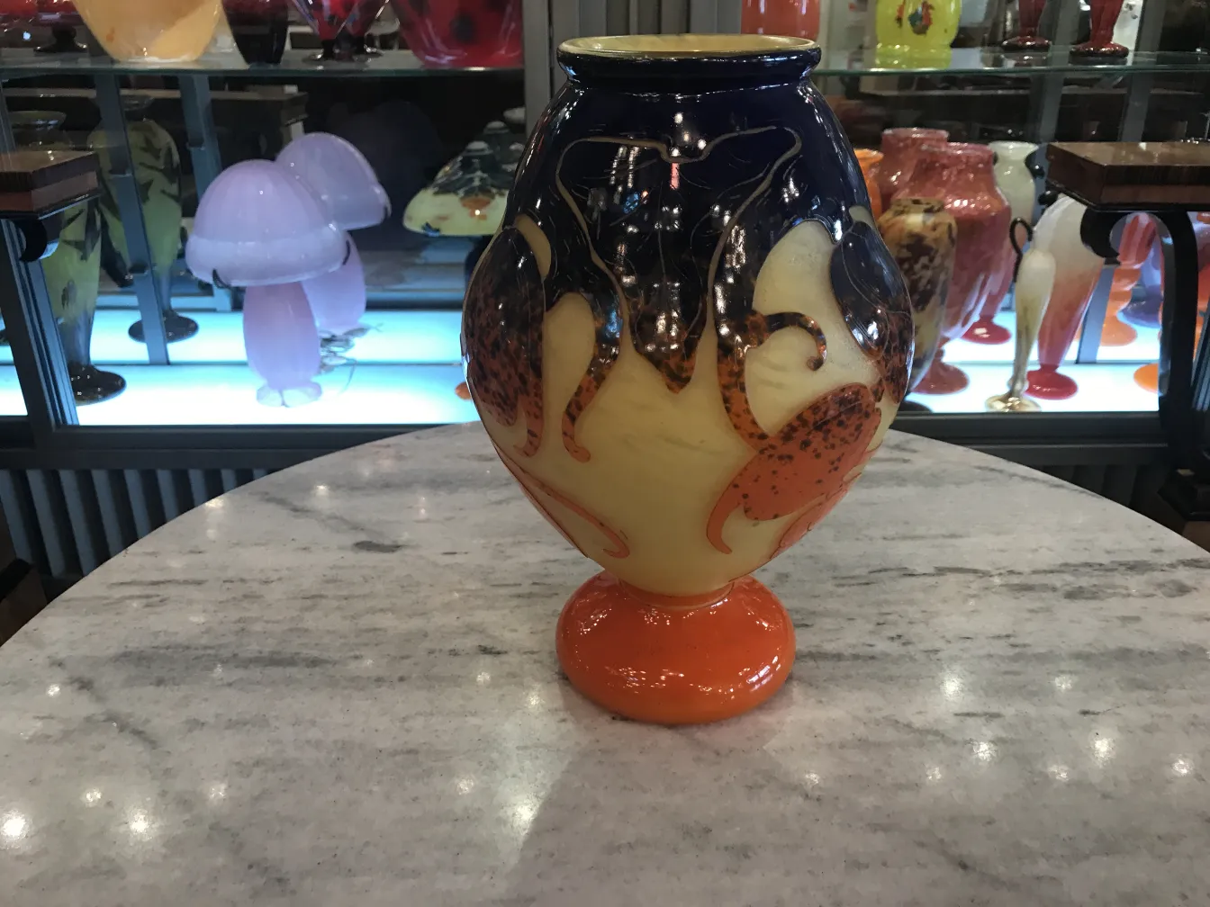 Antique vase with signed glass details in orange and blue, exhibition background.