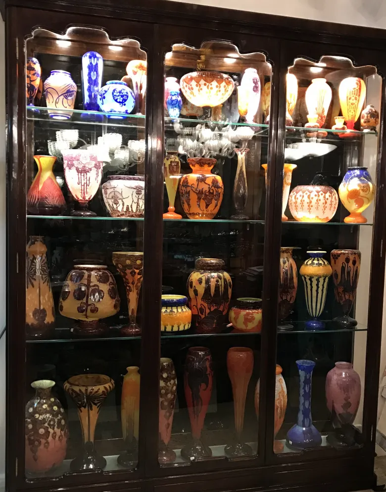 Shelves filled with various antique glass vases, some signed, colorful with intricate patterns.