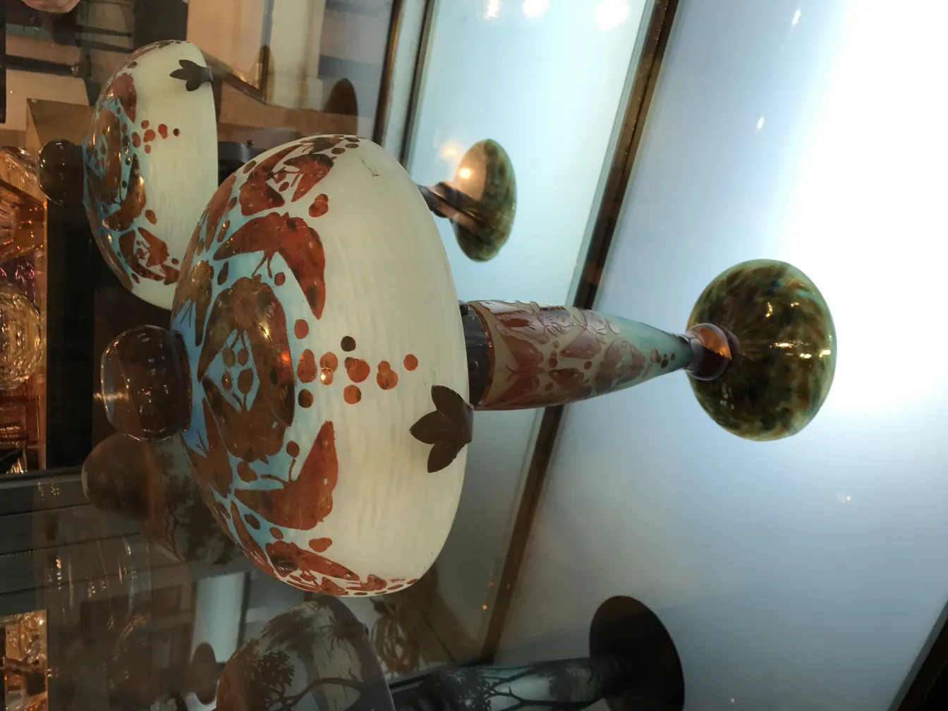 Antique glass piece with decorative details and signature, showcasing vibrant colors, displayed in an elegant setting.