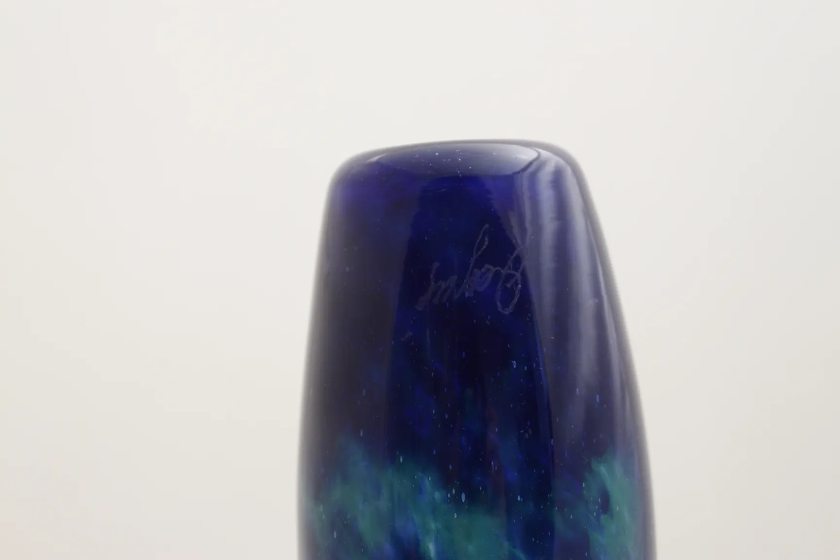 Vidro antigo assinado Degué com tons de azul e verde em um fundo simples.