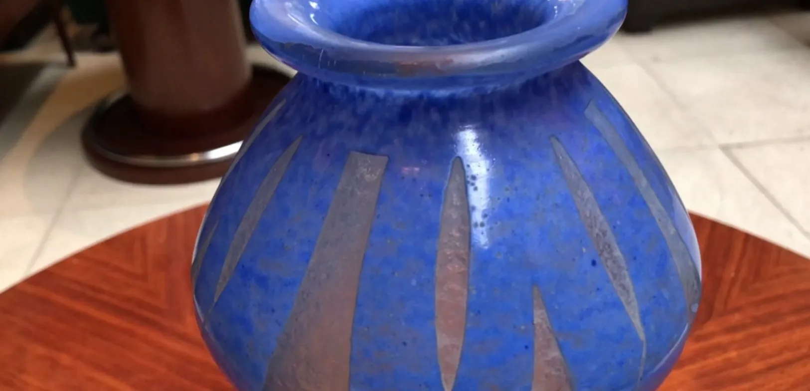 Antigo vaso de vidro azul assinado Degué, decorado com listras, em um ambiente elegante.