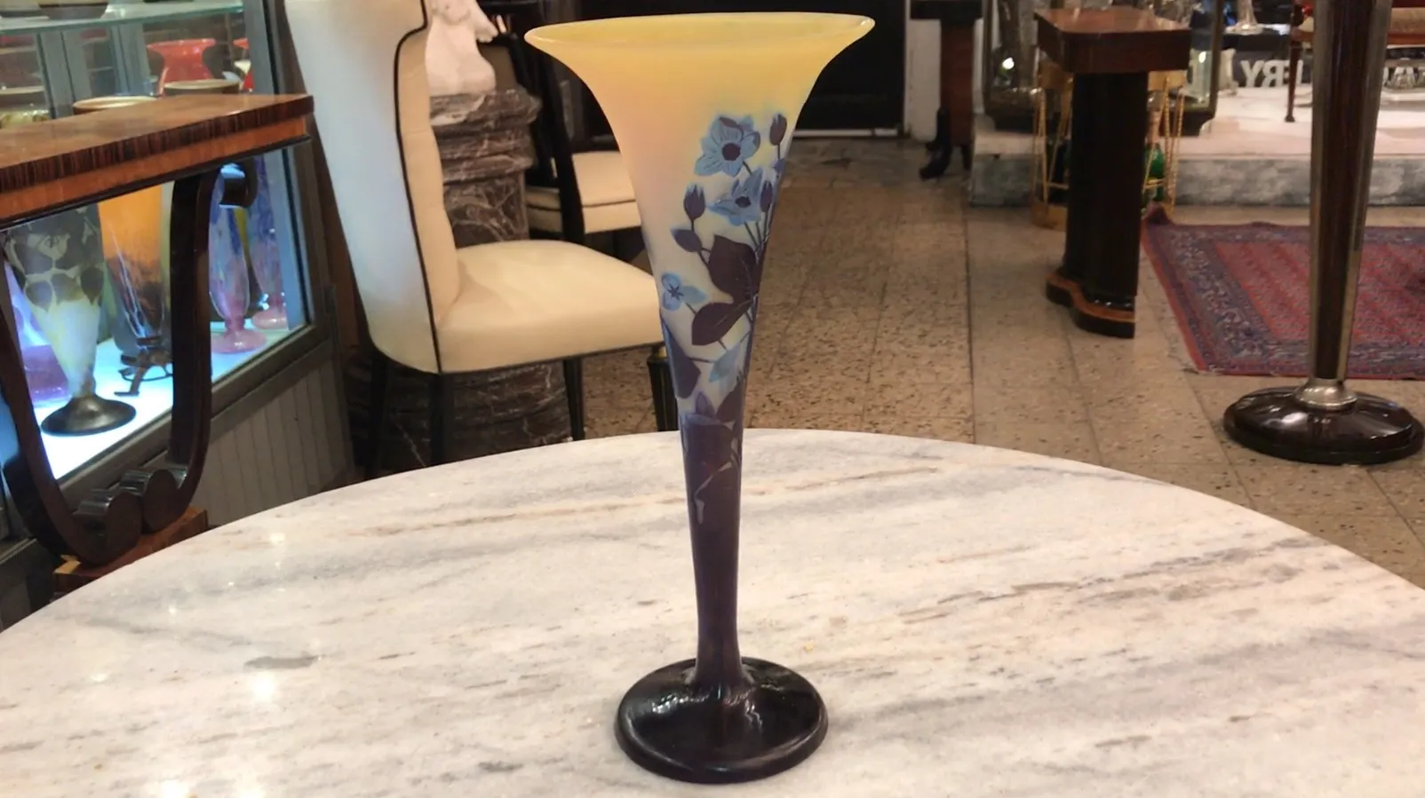 Signed glass Gallé featuring floral design on yellow background, set in an antique environment.